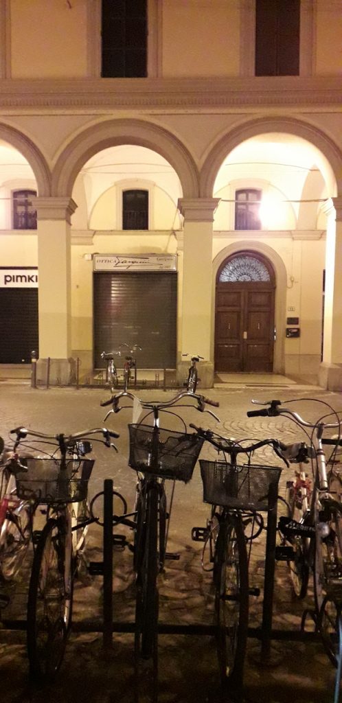 Bikes in front of a Bologna portico at night.
